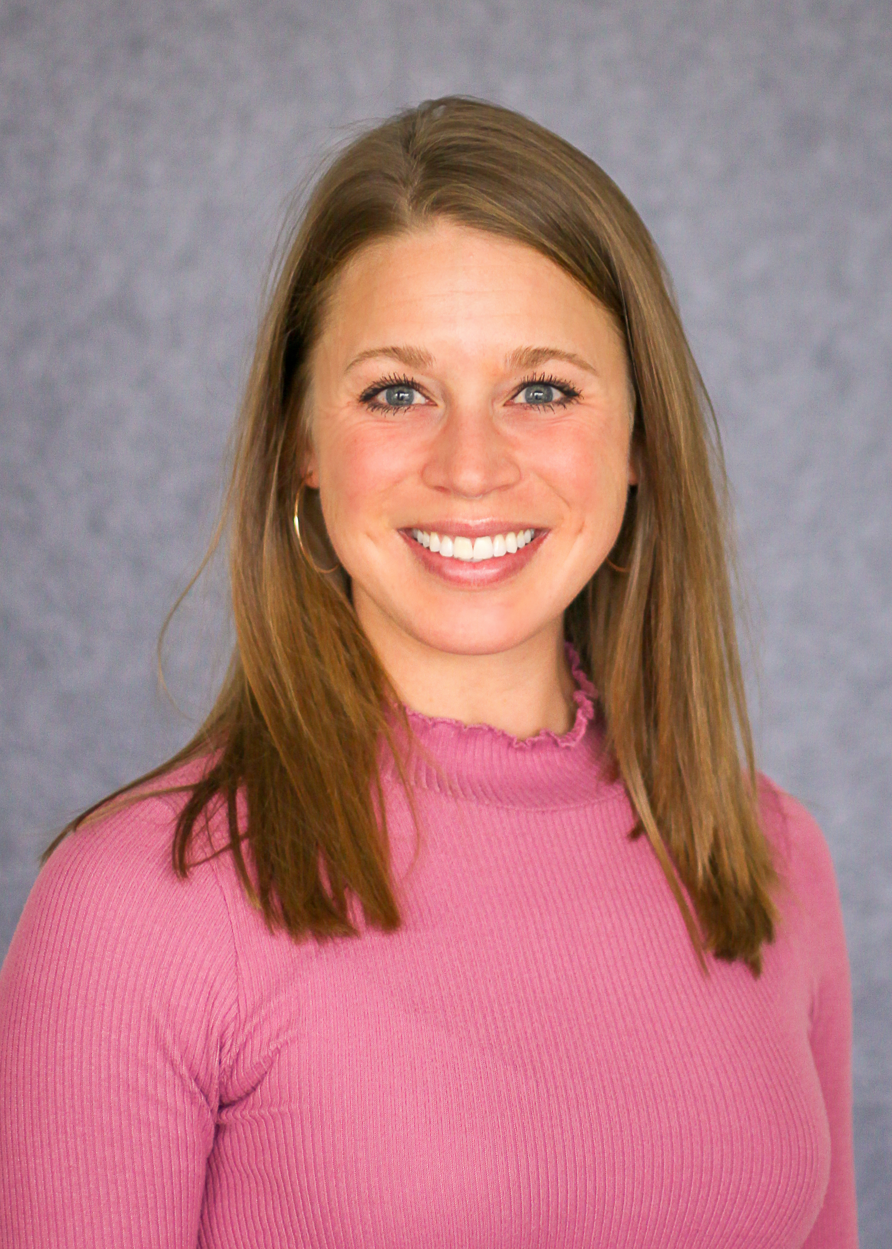 Woman smiling with brown hair wearing a pink sweater