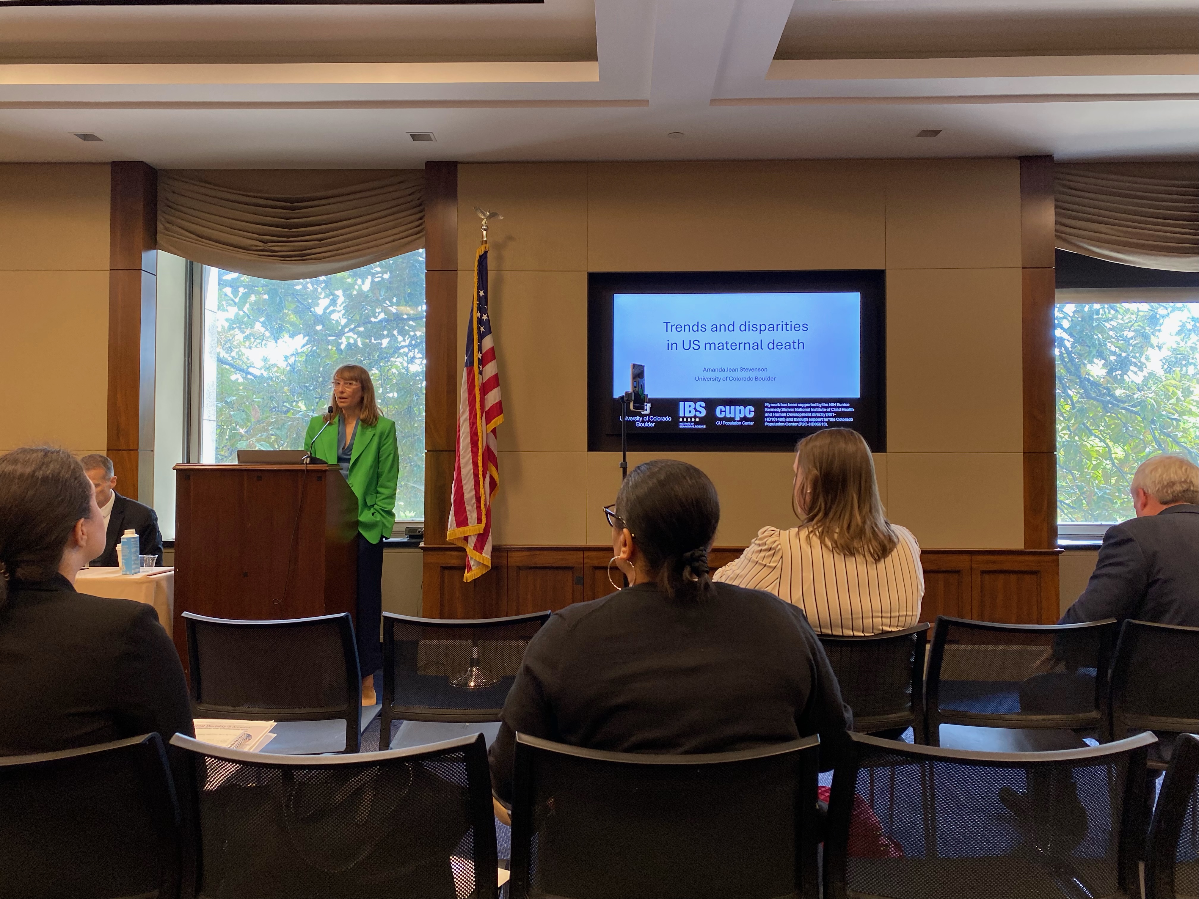 CU Sociology Professor Dr. Amanda Stevenson presenting at a congressional briefing behind a Powerpoint presentation that reads "Trends and disparities in US maternal health"