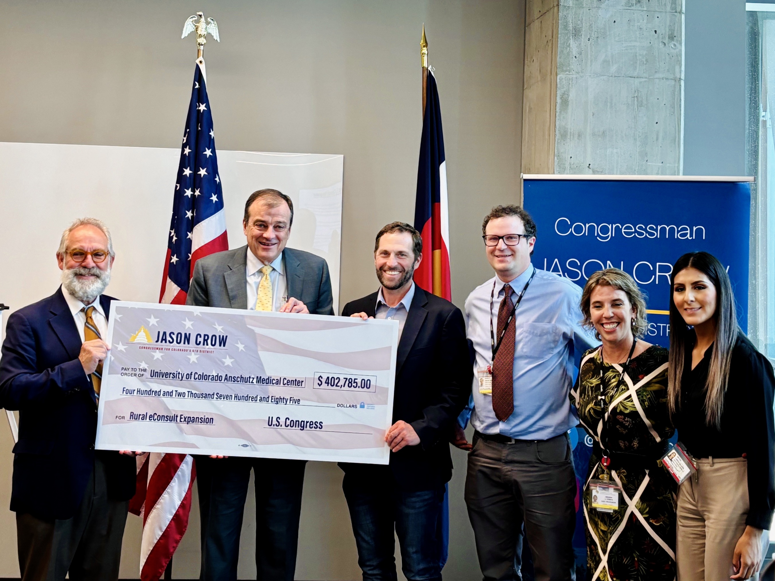 Rep. Jason Crow (D-CO), Dean of the CU School of Medicine John J. Reilly Jr., MD,  and staff with the CU School of Medicine Peer Mentored Care Collaborative (PMCC) holding an oversized check for $402,785 from the U.S. Congress to CU Anschutz for the Rural eConsult Expansion